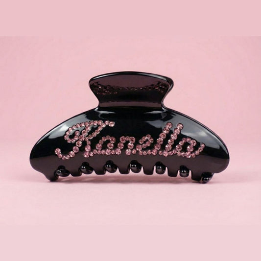 Black hair clip with 'Kanella' branding on a pink background